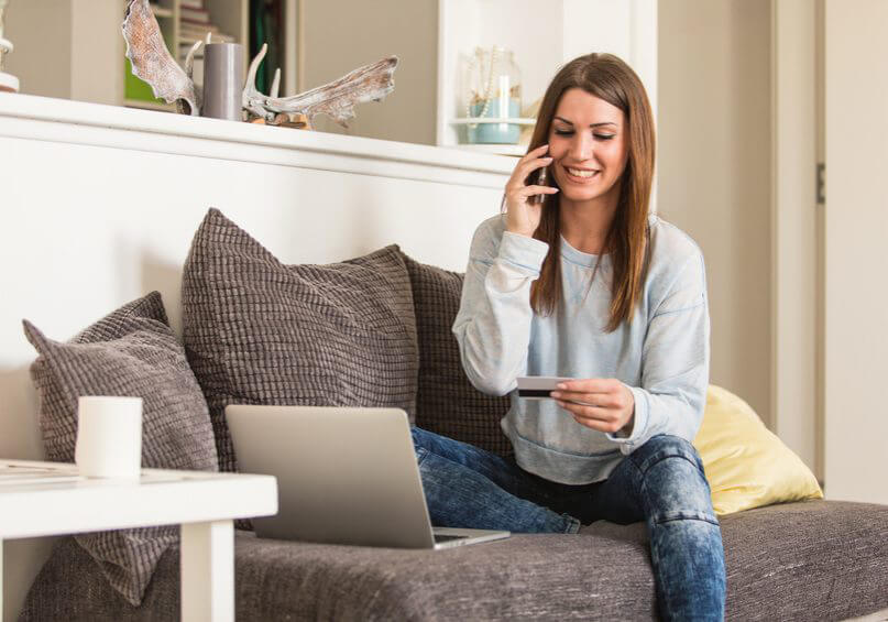 Woman shopping from home, talking on the mobile phone Young woman holding credit card and using laptop at home